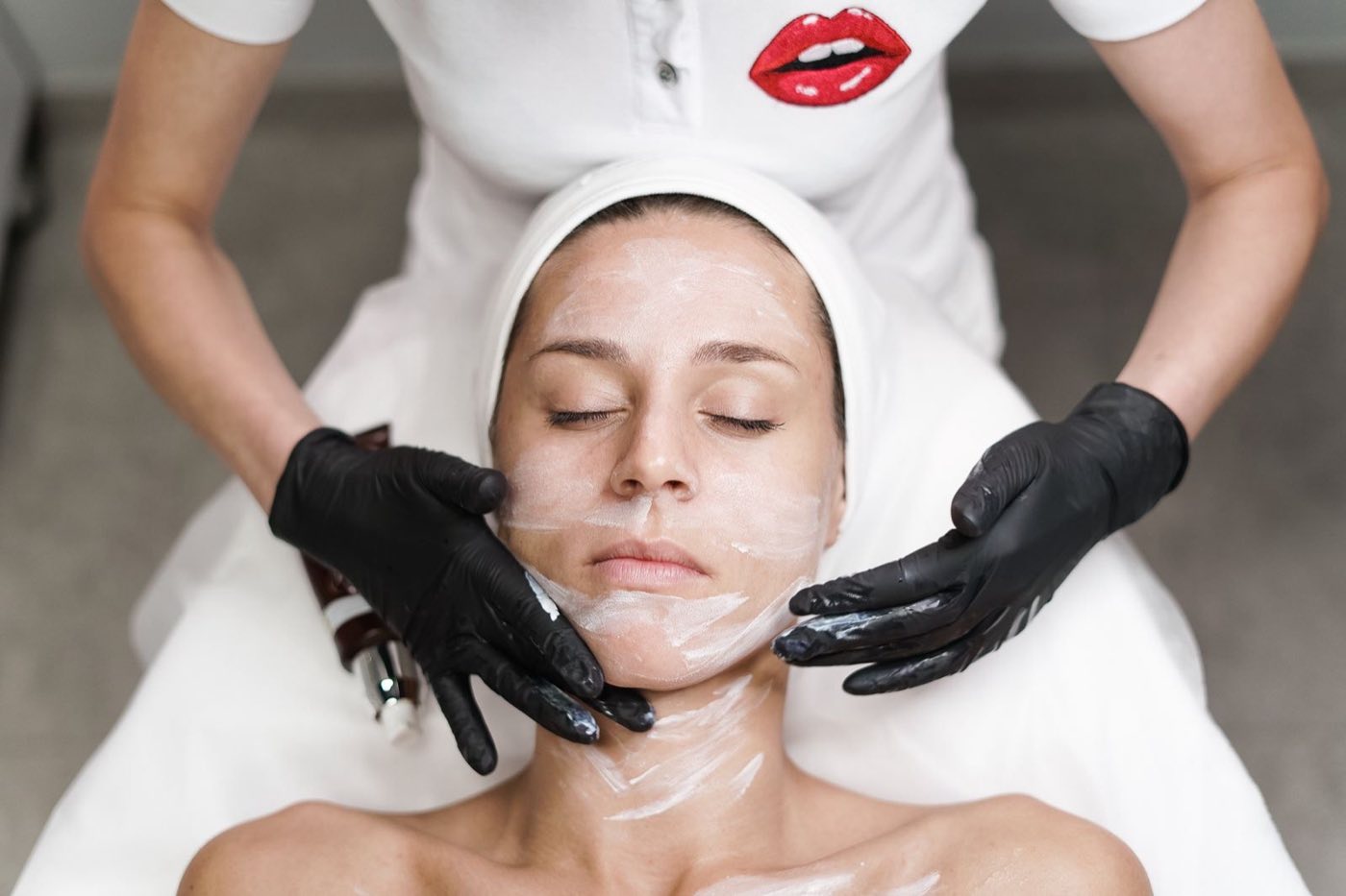 Esteticista aplicando máscara facial em cliente durante procedimento de limpeza de pele